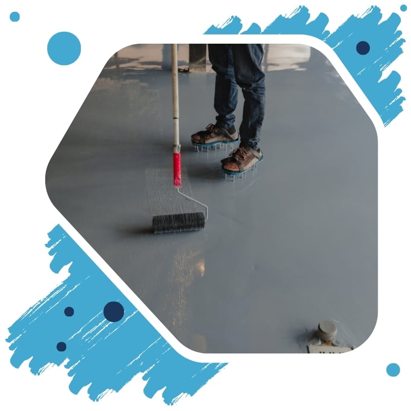 The worker uses a long roller to apply gray epoxy resin to the new floor.