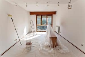 Interior of a room in progress of being prepped for painting. The room is covered in plastic sheeting and a paint ladder stands in the background.