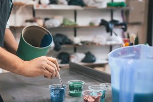 Person using leftover paint in various colors, with a brush and containers on a workbench in a creative studio, illustrating leftover paint ideas for DIY projects.