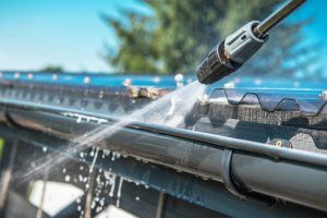 Close-up of a pressure washer cleaning a corrugated metal roof to prevent roof crack paint issues, demonstrating maintenance tips for a healthy roof.