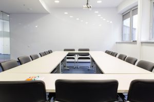 A modern conference room with a large U-shaped table, black chairs, and a whiteboard wall painted with writable paint for walls, showcasing a clean and functional office space.