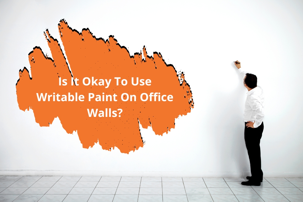 A man in a white shirt writes on a blank white wall with an orange paint splash graphic containing the text 'Is It Okay To Use Writable Paint On Office Walls?' - highlighting the use of writable paint for walls in office settings.