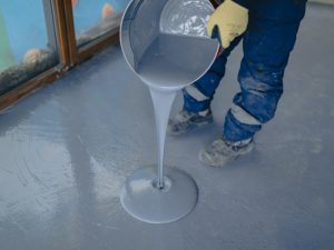 A homeowner pouring epoxy mixture onto a floor, showing how to create DIY epoxy floors on various flooring surfaces.