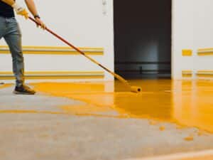 Person struggling to apply paint to a garage floor, paint not sticking properly.