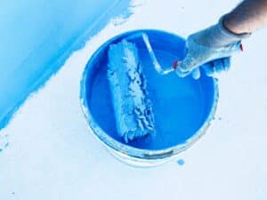 Paint roller with blue paint to remove pool paint and apply fresh coating.