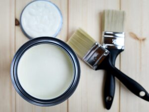 Open paint can with brushes on a wooden surface, showcasing tools used to avoid paint cracking issues.