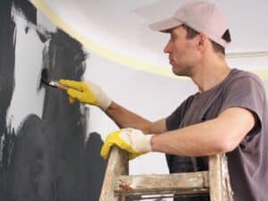 A man on a ladder painting an interior wall black, ensuring smooth application to avoid bubbling paint issues.