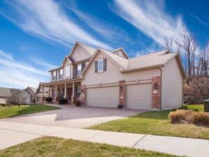 A two-storey house with a brick driveway and two garage doors. Considering the house painting cost.