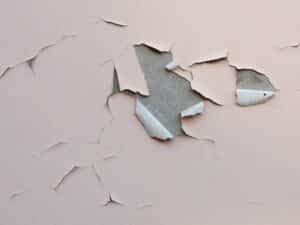 Cracked and peeling pink paint shows poor paint maintenance on a wall.