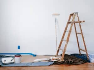 Setup for new home painting showing ladder, roller, and tools in front of blank white wall.