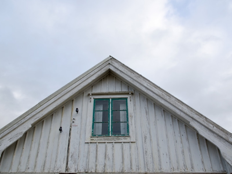 Exterior damage on houses that need painting with peeling paint on weatherboard gable