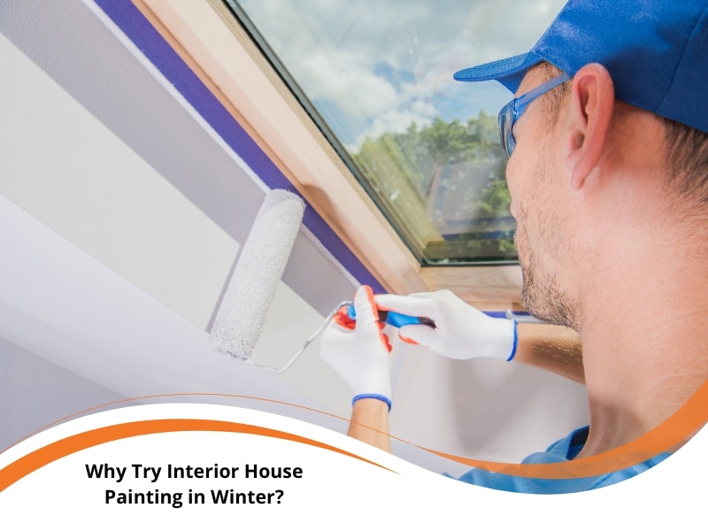 Professional painter applying white paint with roller near window during interior house painting in winter conditions.
