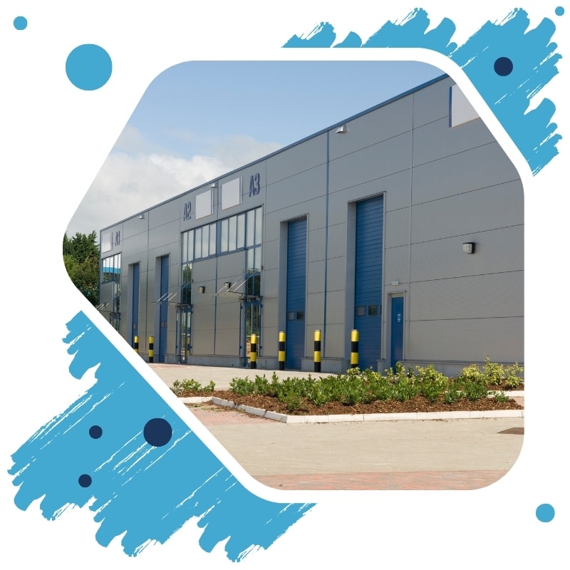 Modern grey warehouse with blue roller doors after commercial painting in Sydney, featuring clean facade and landscaping.