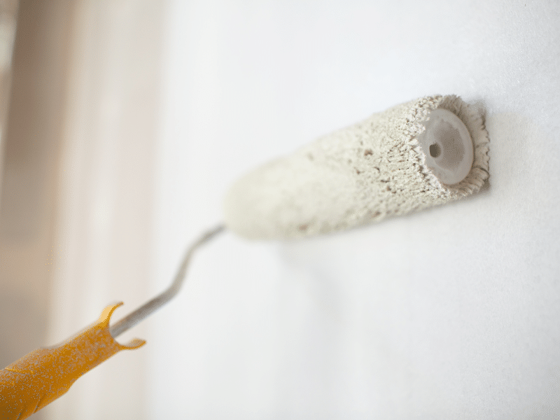 Interior paint contractors using a roller brush for even wall coating. 