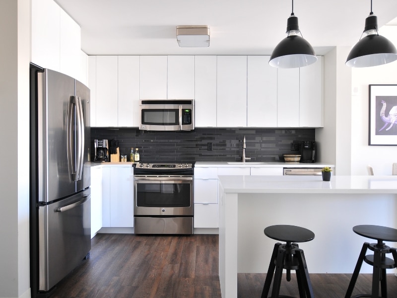 A stylish kitchen featuring stainless steel refrigerator and oven, white cabinetry, and dark backsplash, offering a perfect canvas for kitchen painting enhancements.