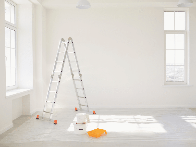Interior paint contractors set up a ladder and supplies in a bright room. 