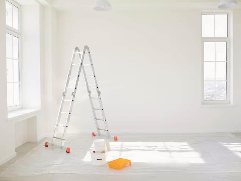 Ladder and paint tools prepared for professional wall painting project in white room.