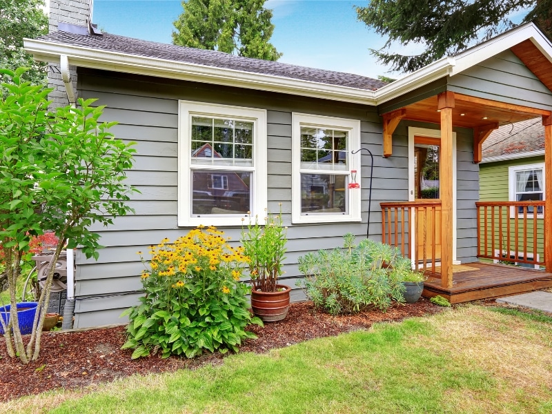 Grey exterior walls paint colours on small house with wooden porch and garden