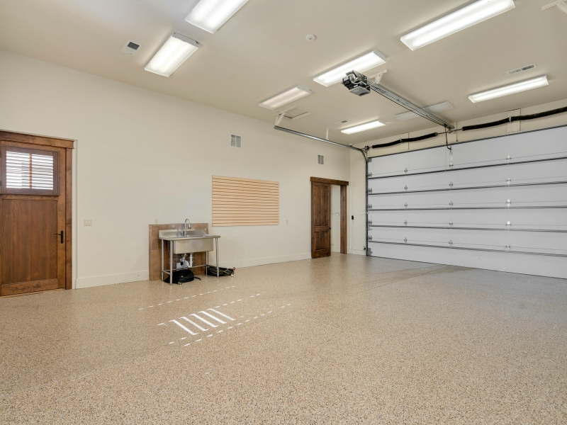 Spacious garage with epoxy floor featuring bright lighting, wooden doors, and a stainless steel sink area.